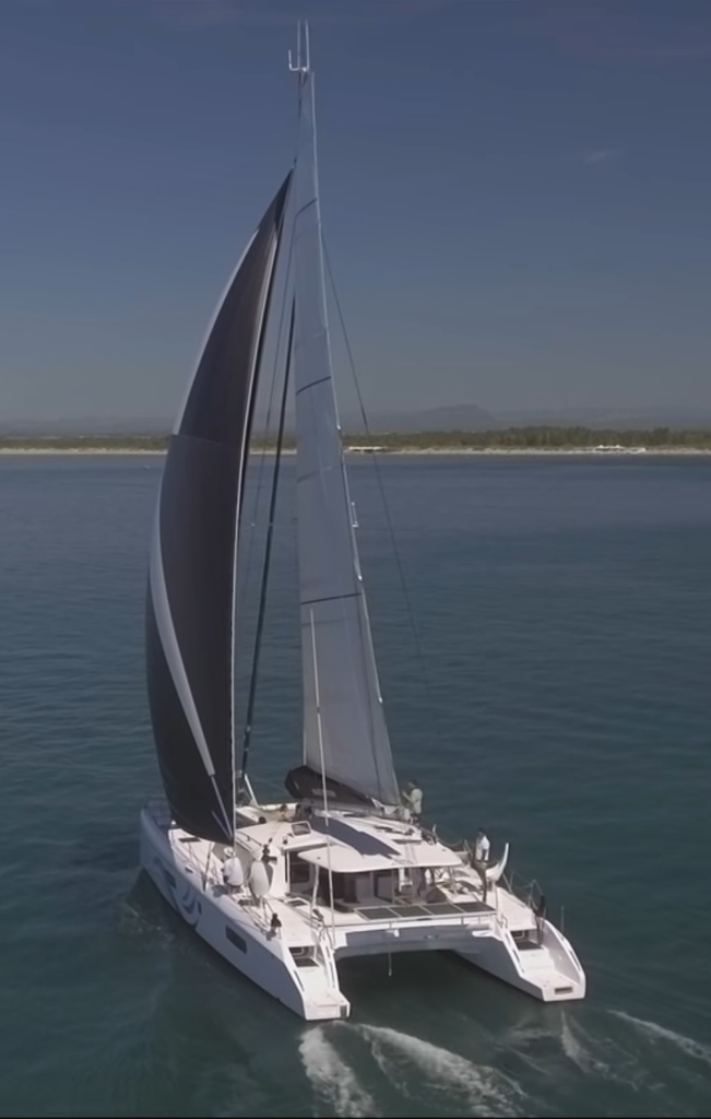 A white Outremer sailing catamaran under full sail on open water.