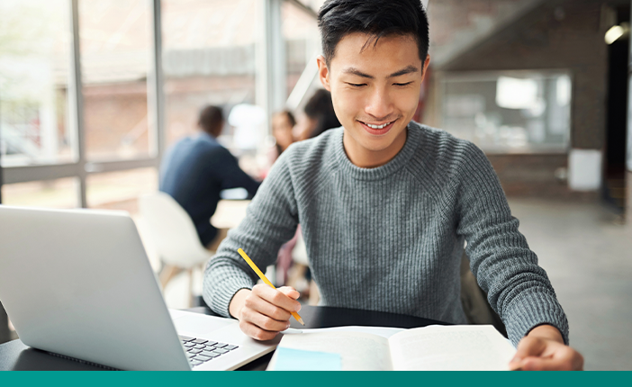 A student sitting at a table with a computer and a book