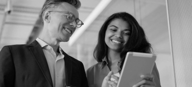 A man and a woman smiling and looking at a tablet.