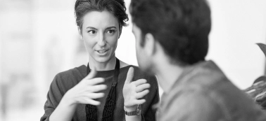 A woman explains something to a man in a work meeting.