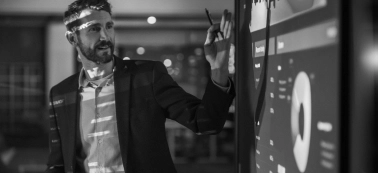 A man explaining something and looking at a big screen in a work meeting.