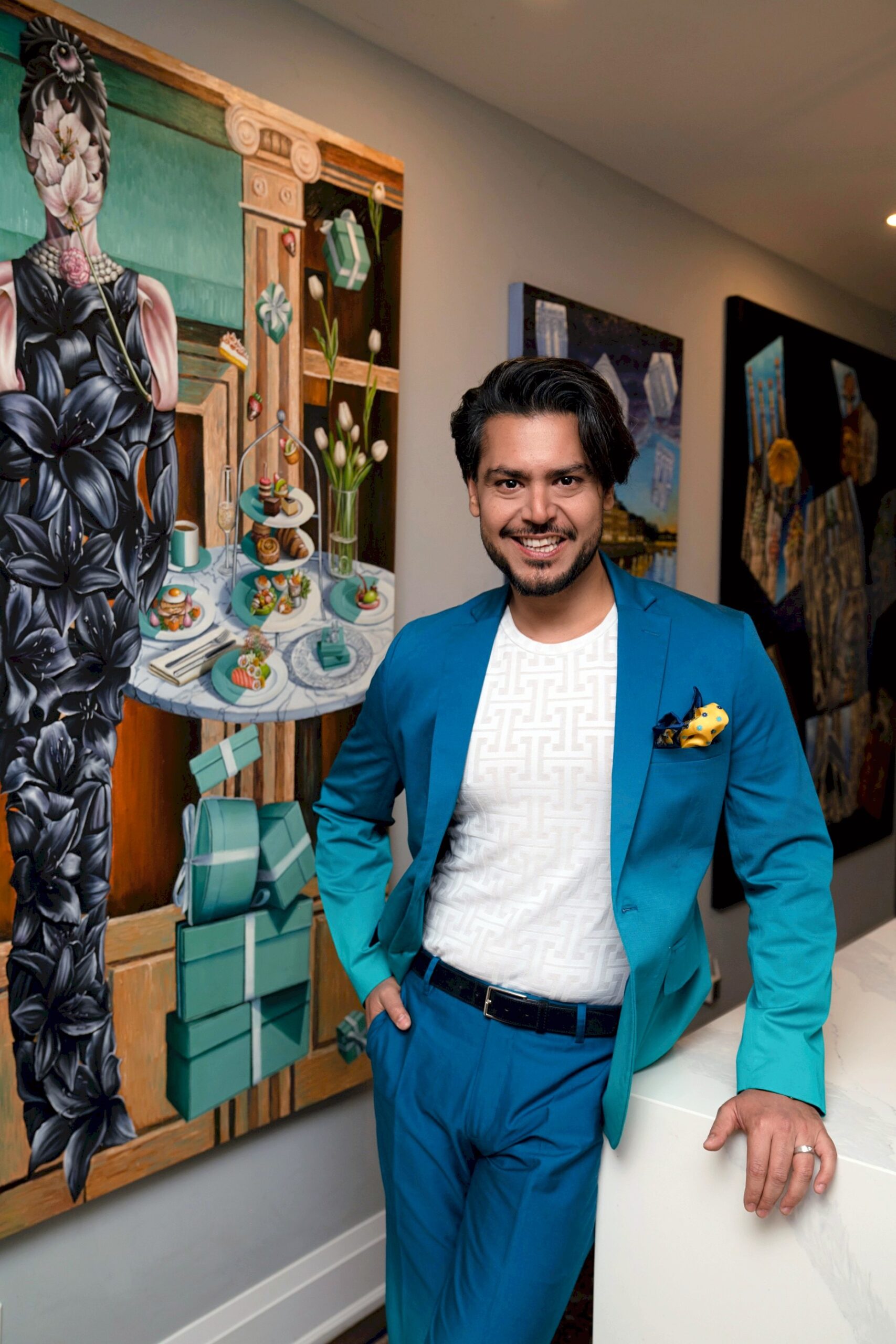 Actuary and artist Haris Sardar in a teal suit, standing in an art gallery beside his paintings.