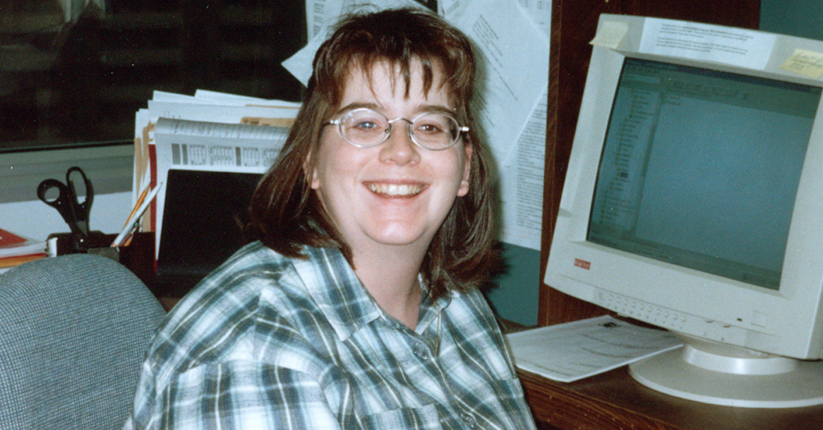 A young Lynn Blackburn, wearing glasses and a plaid shirt, seated at a desk with a vintage computer monitor in her early days at the CIA (1990s).